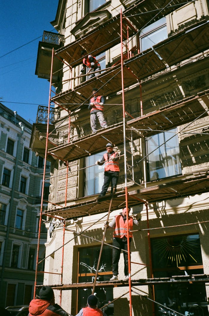 about-02 Construction workers on scaffolding renovating a building facade on a sunny day.