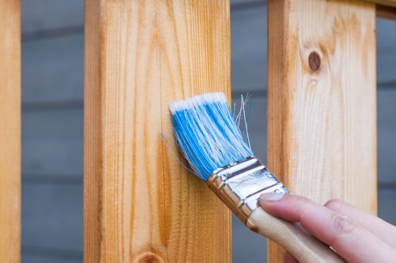 why-choose-us-02 A hand painting a wooden fence plank with a blue paintbrush outdoors. Perfect for DIY and renovation themes.